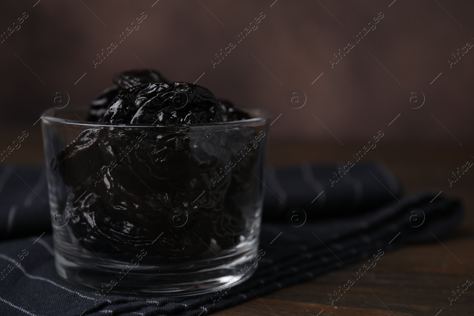 Photo of Tasty dried plums (prunes) in glass bowl on wooden table, closeup. Space for text