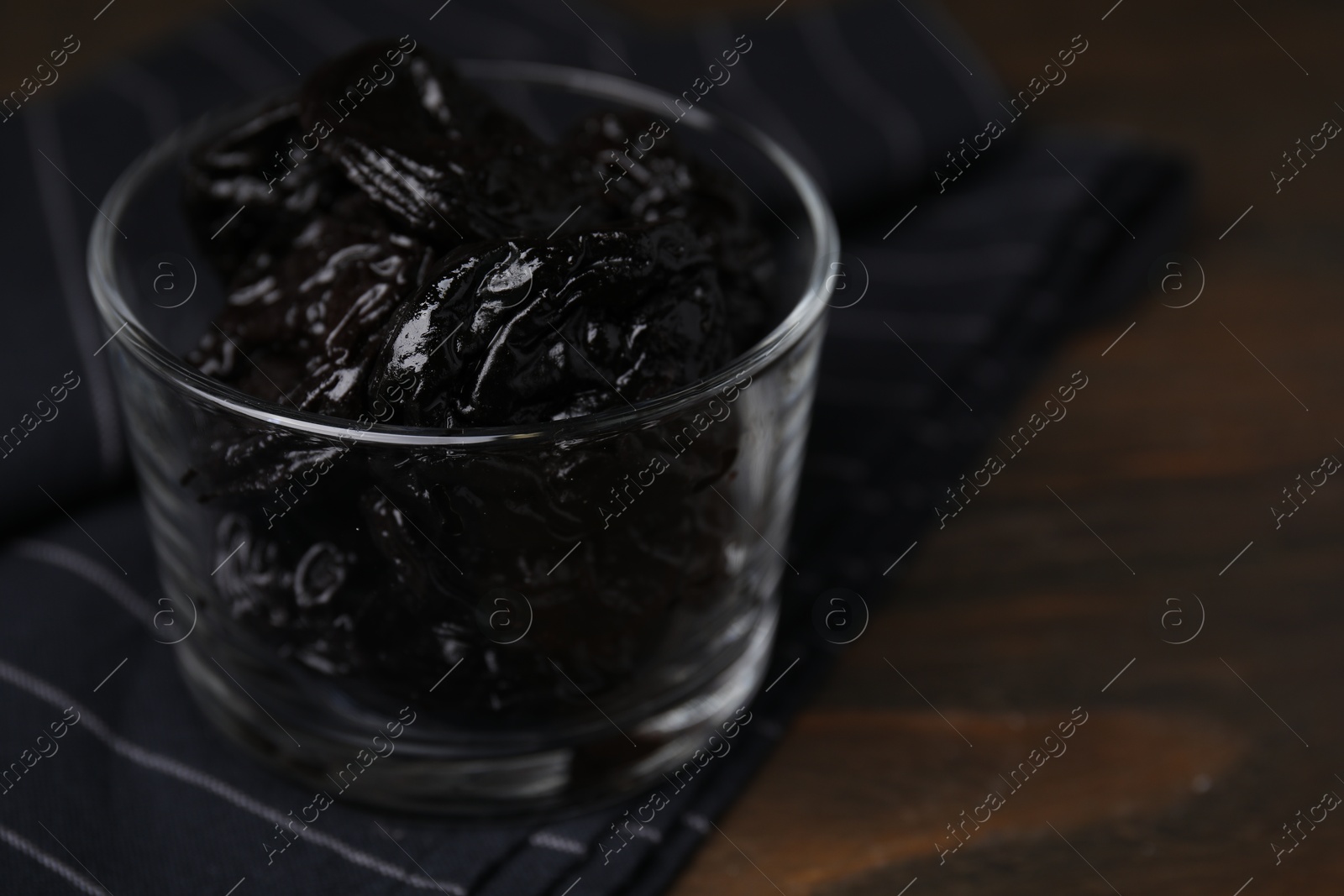 Photo of Tasty dried plums (prunes) in glass bowl on wooden table, closeup. Space for text