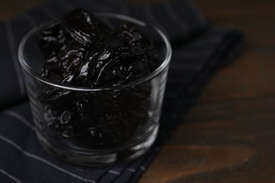 Tasty dried plums (prunes) in glass bowl on wooden table, closeup. Space for text