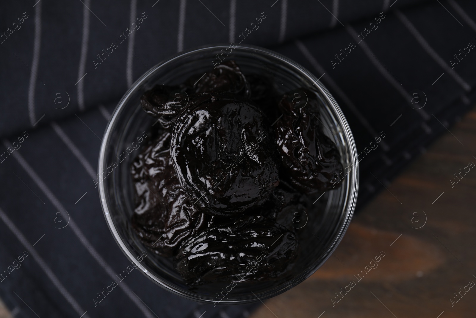 Photo of Tasty dried plums (prunes) in glass bowl on wooden table, top view