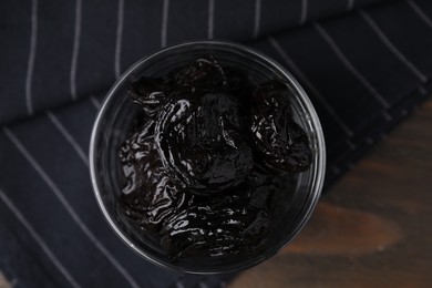 Tasty dried plums (prunes) in glass bowl on wooden table, top view