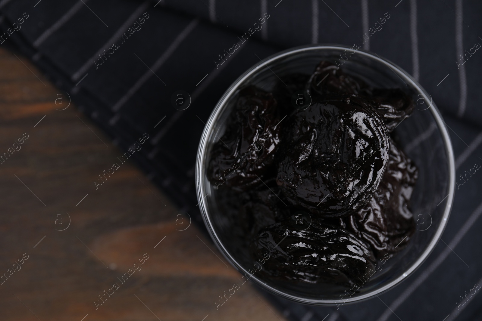 Photo of Tasty dried plums (prunes) in glass bowl on wooden table, top view. Space for text