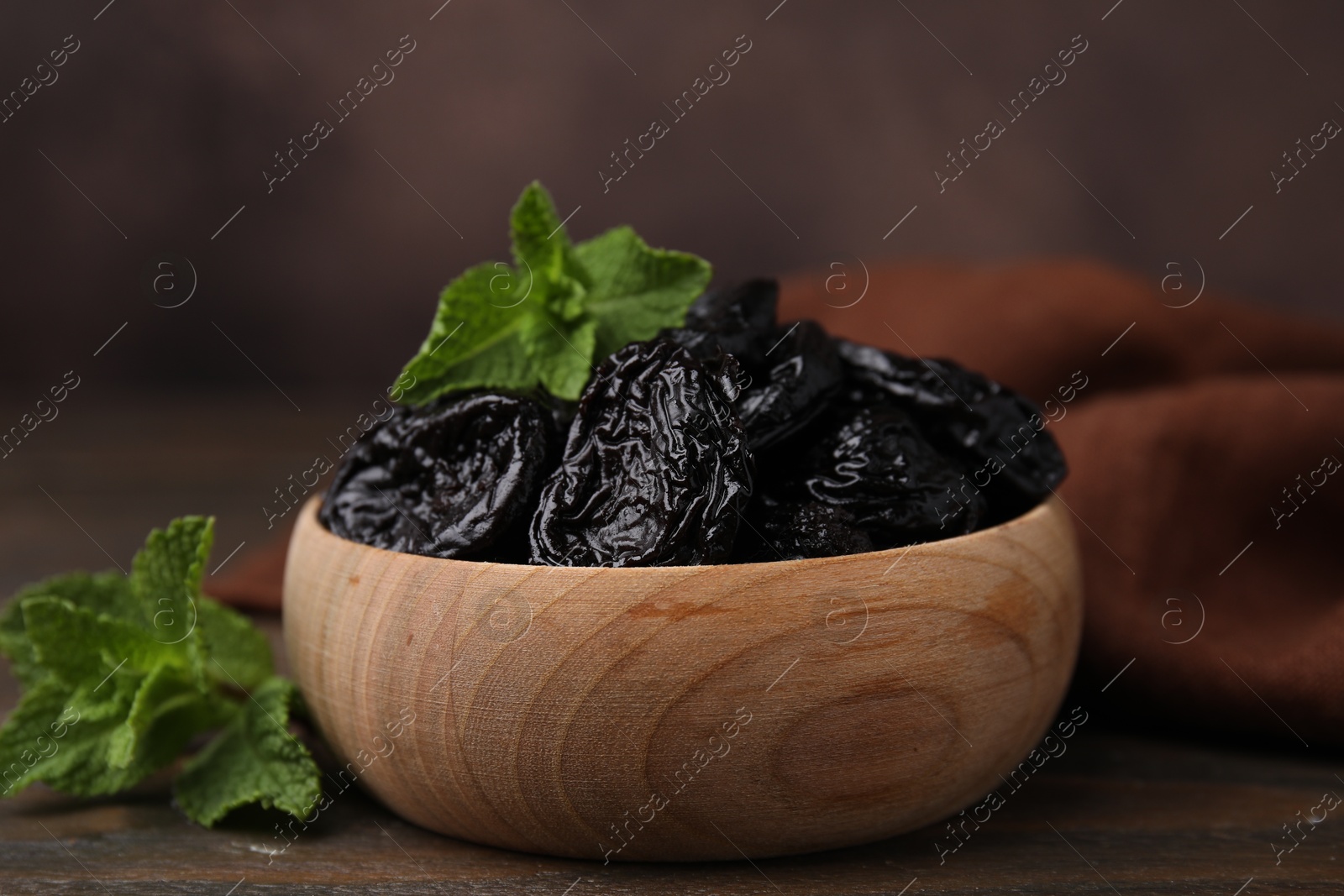 Photo of Tasty dried plums (prunes) and mint leaves in bowl on wooden table, closeup