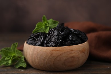 Tasty dried plums (prunes) and mint leaves in bowl on wooden table, closeup