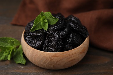 Photo of Tasty dried plums (prunes) and mint leaves in bowl on wooden table, closeup