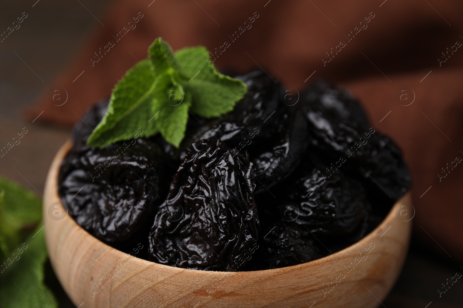 Photo of Tasty dried plums (prunes) and mint leaves in wooden bowl, closeup