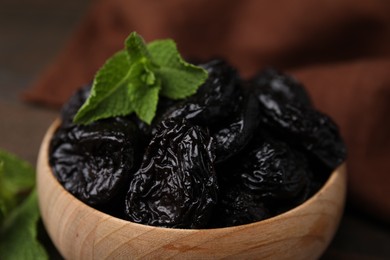 Tasty dried plums (prunes) and mint leaves in wooden bowl, closeup