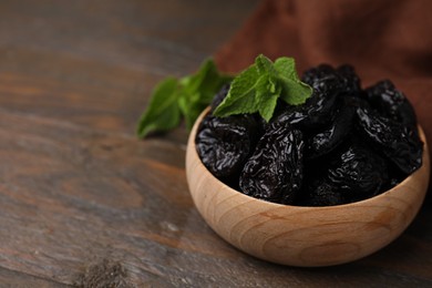 Tasty dried plums (prunes) and mint leaves in bowl on wooden table, closeup. Space for text