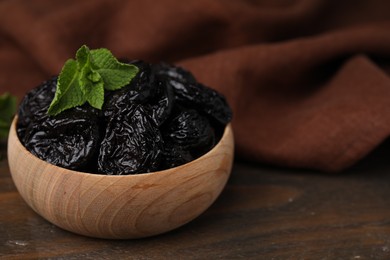 Photo of Tasty dried plums (prunes) and mint leaves in bowl on wooden table, closeup. Space for text