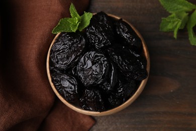 Photo of Tasty dried plums (prunes) and mint leaves in bowl on wooden table, flat lay