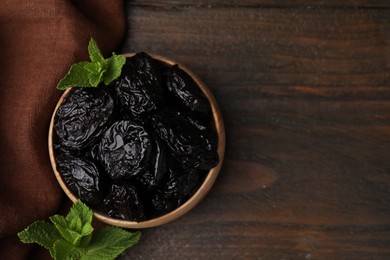 Photo of Tasty dried plums (prunes) and mint leaves in bowl on wooden table, flat lay. Space for text