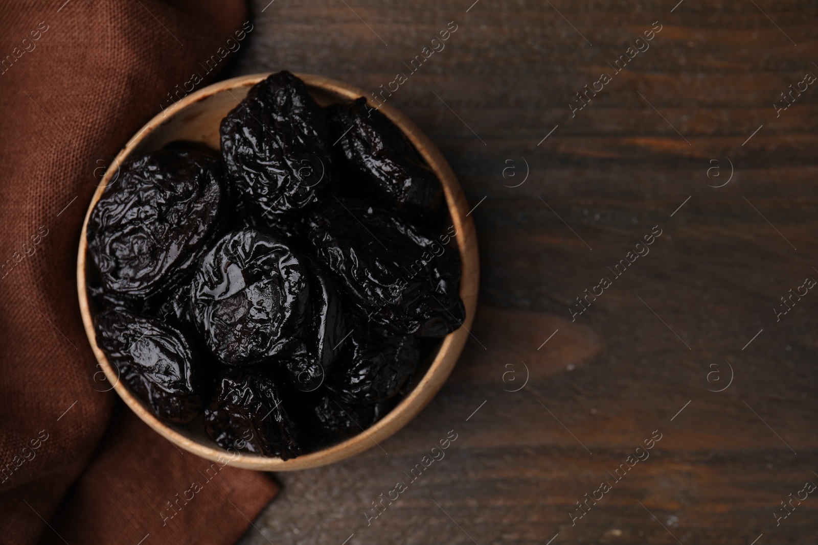 Photo of Tasty dried plums (prunes) in bowl on wooden table, top view. Space for text