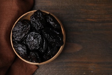 Photo of Tasty dried plums (prunes) in bowl on wooden table, top view. Space for text