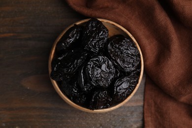 Photo of Tasty dried plums (prunes) in bowl on wooden table, top view