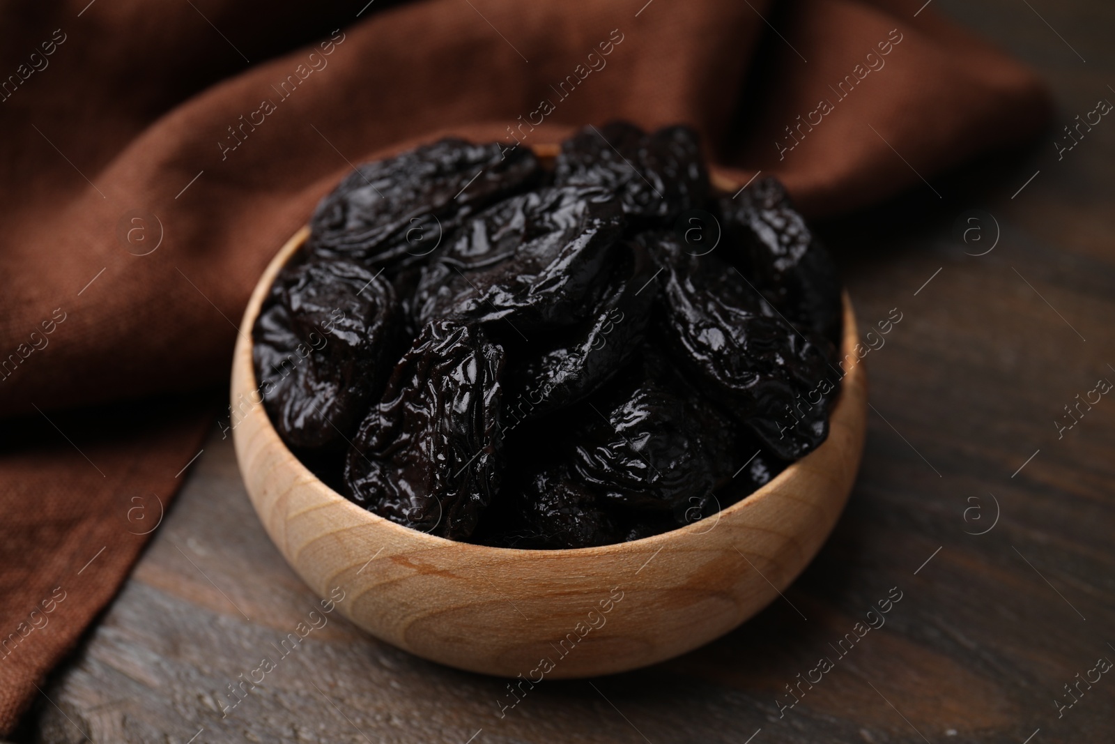 Photo of Tasty dried plums (prunes) in bowl on wooden table, closeup