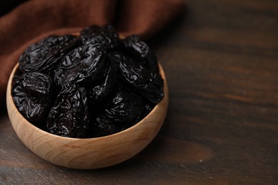Photo of Tasty dried plums (prunes) in bowl on wooden table, closeup. Space for text