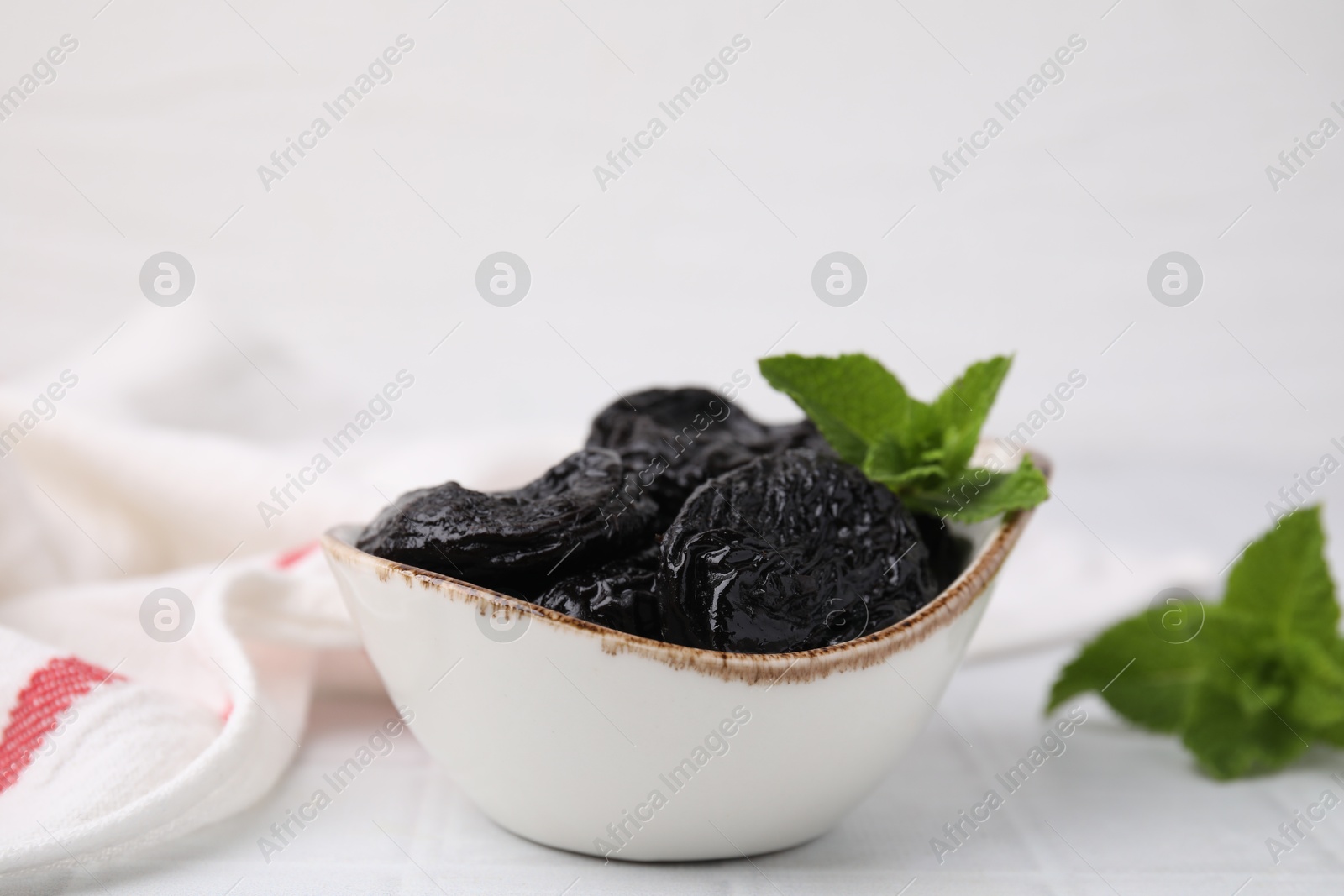 Photo of Tasty dried plums (prunes) and mint leaves on white table, closeup