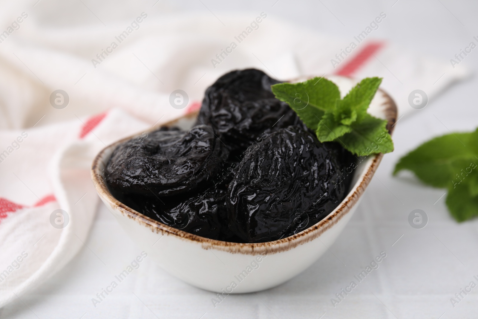 Photo of Tasty dried plums (prunes) and mint leaves on white table, closeup