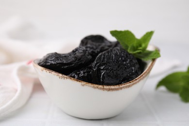 Tasty dried plums (prunes) and mint leaves on white table, closeup