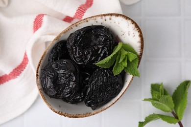 Tasty dried plums (prunes) and mint leaves on white tiled table, flat lay