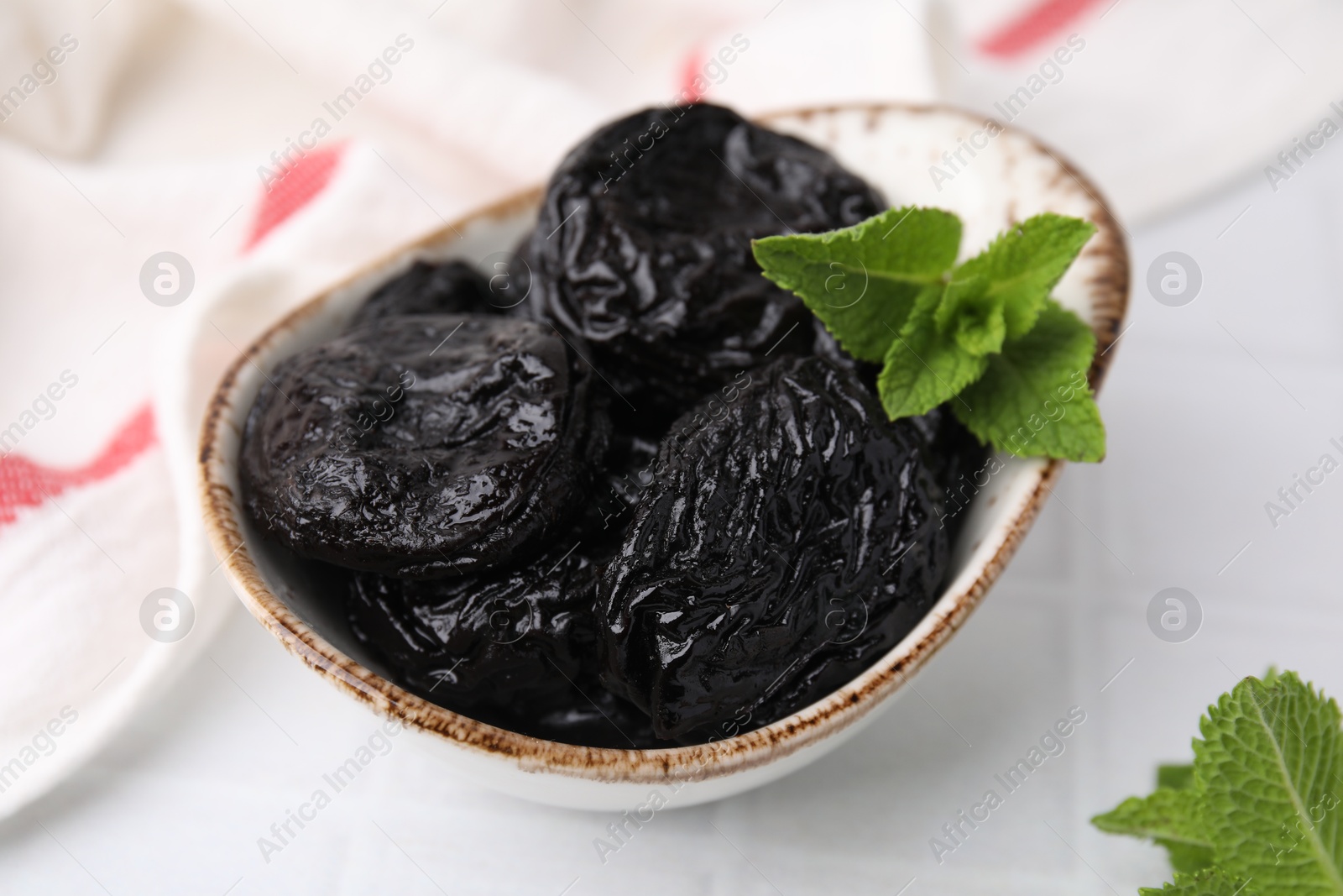 Photo of Tasty dried plums (prunes) and mint leaves on white table, closeup