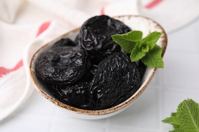 Photo of Tasty dried plums (prunes) and mint leaves on white table, closeup