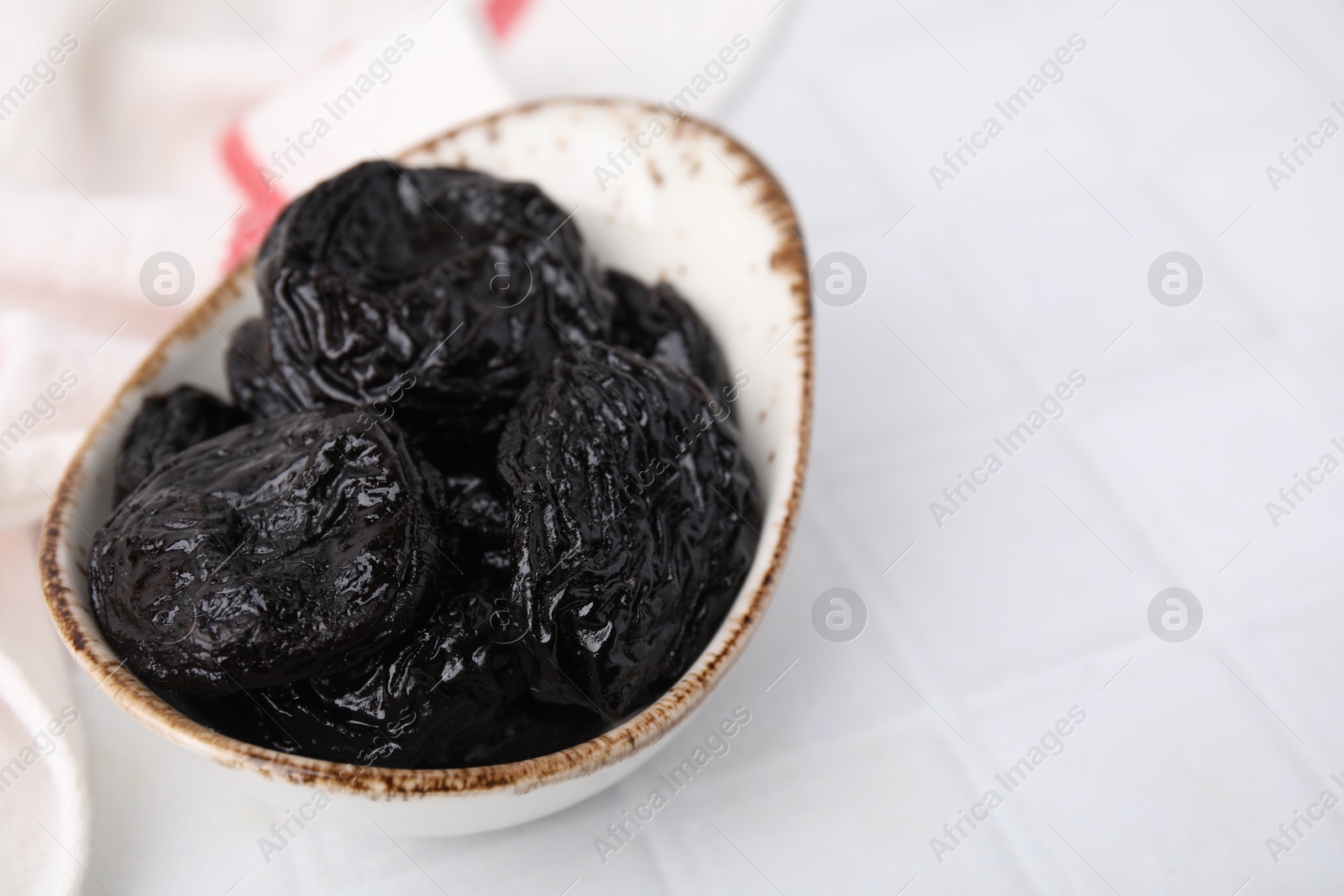 Photo of Tasty dried plums (prunes) on white tiled table, closeup. Space for text