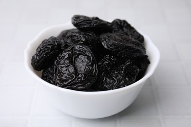 Tasty dried plums (prunes) in bowl on white tiled table, closeup