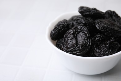 Photo of Tasty dried plums (prunes) in bowl on white tiled table, closeup. Space for text
