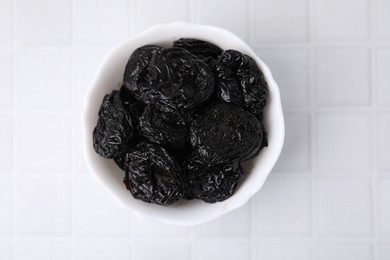 Tasty dried plums (prunes) in bowl on white tiled table, top view