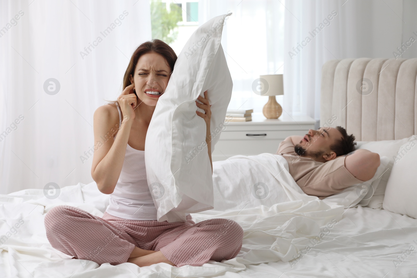 Photo of Bedtime. Irritated woman covering ears near her snoring husband in bed at home