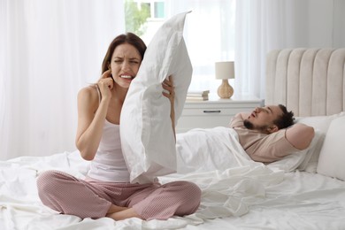 Photo of Bedtime. Irritated woman covering ears near her snoring husband in bed at home