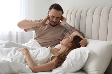 Photo of Bedtime. Irritated man covering ears near his snoring wife in bed at home