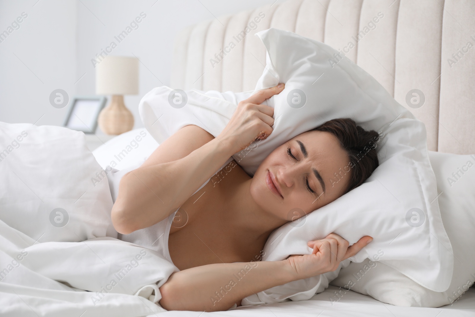 Photo of Woman covering ears with pillow in bed at morning