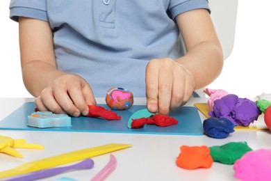 Photo of Little boy sculpting with play dough at table on white background, closeup