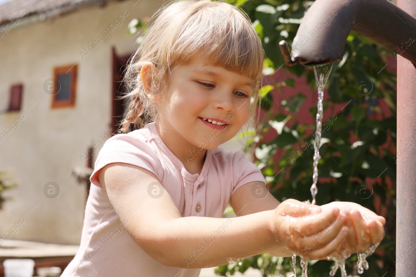 Photo of Water scarcity. Cute little girl drawing water with hands from tap outdoors