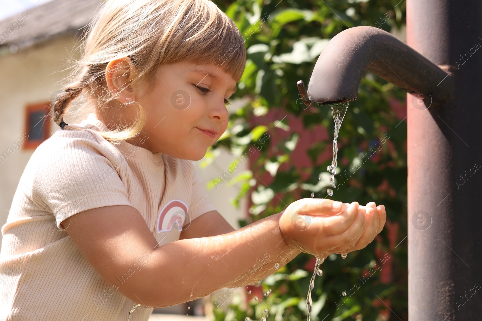 Photo of Water scarcity. Cute little girl drawing water with hands from tap outdoors