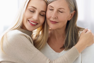 Family portrait of young woman and her mother on light background