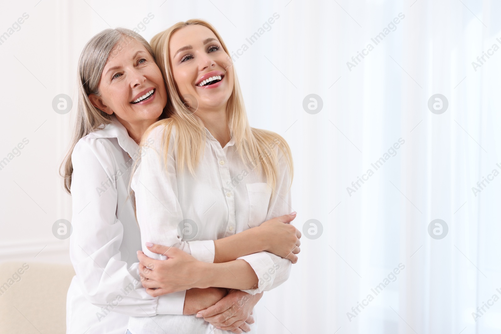 Photo of Family portrait of young woman and her mother near white wall. Space for text