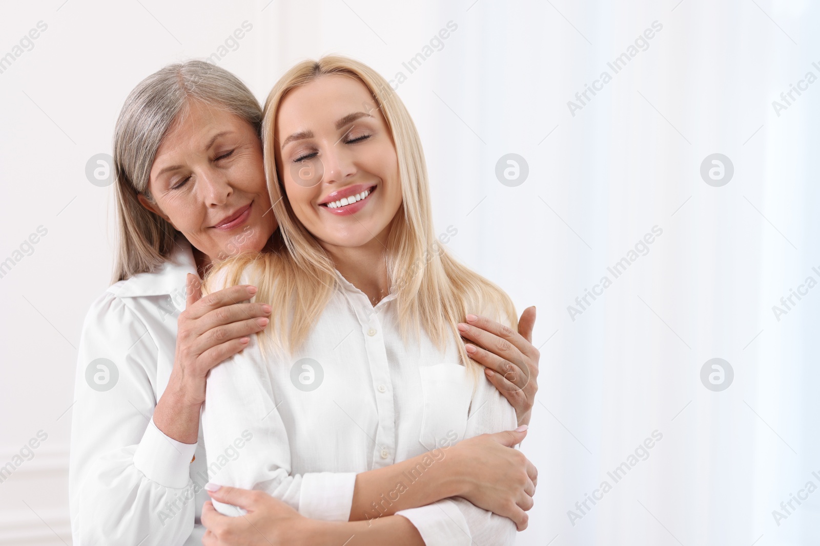 Photo of Family portrait of young woman and her mother near white wall. Space for text