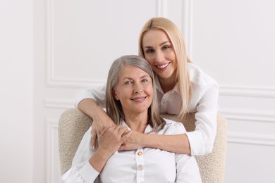 Family portrait of young woman and her mother near white wall