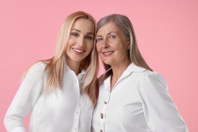 Family portrait of young woman and her mother on pink background