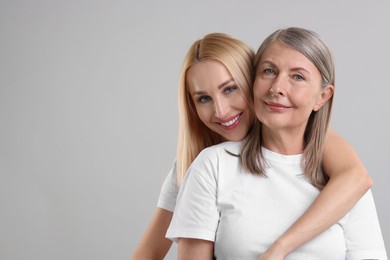Family portrait of young woman and her mother on light grey background. Space for text
