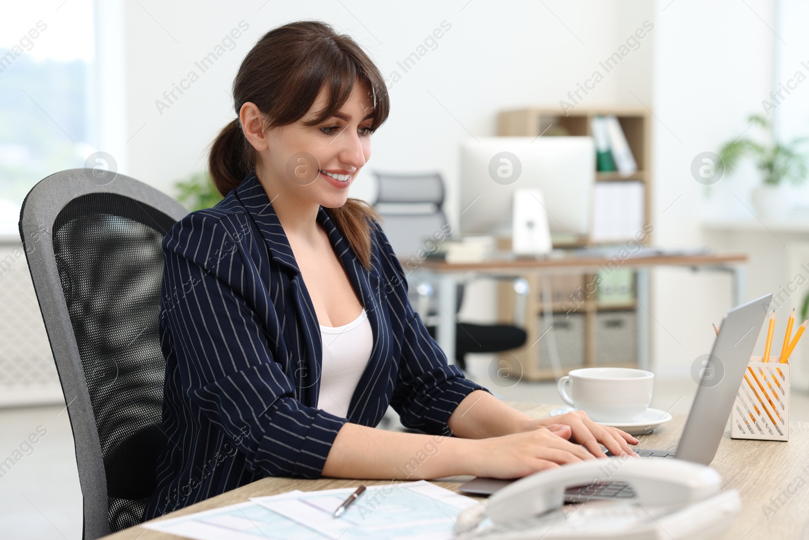 Photo of Smiling secretary typing on laptop at table in office