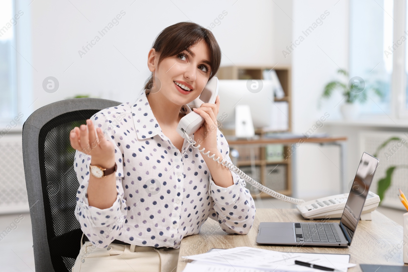 Photo of Smiling secretary talking on telephone at table in office