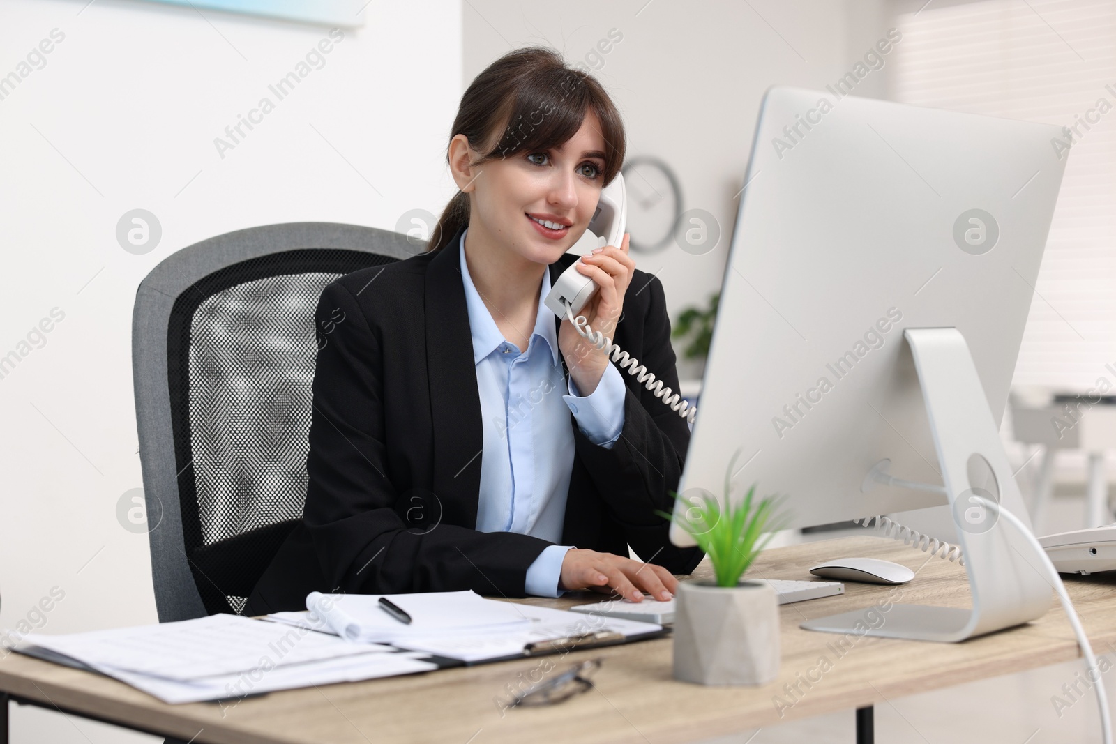 Photo of Smiling secretary talking on telephone at table in office