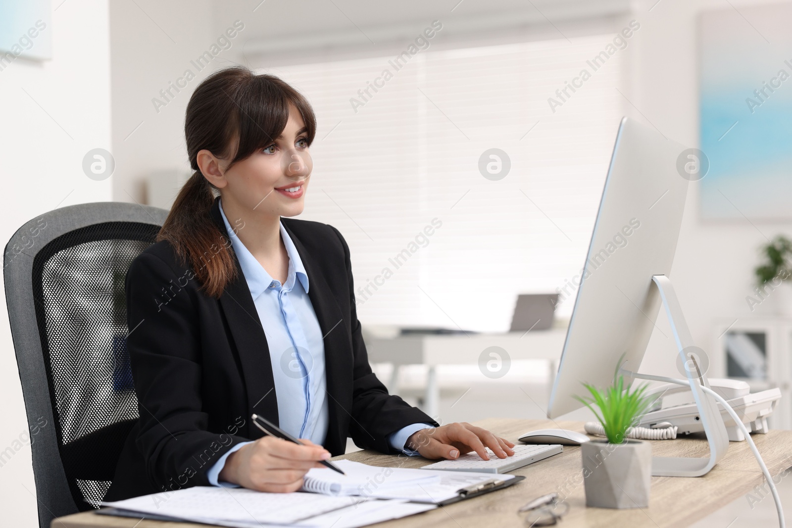 Photo of Smiling secretary working at table in office