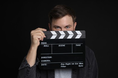 Photo of Making movie. Man with clapperboard on black background