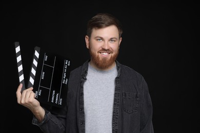 Photo of Making movie. Smiling man with clapperboard on black background