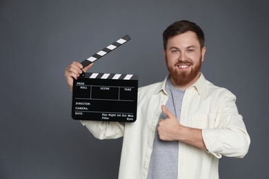 Photo of Making movie. Smiling man with clapperboard showing thumb up on grey background. Space for text